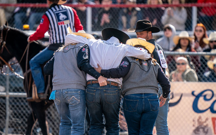 Two JST ladies and a steer wrestler, Jacob Edler, walking out of the arena, the two men holding the middle man helping him after an injury.